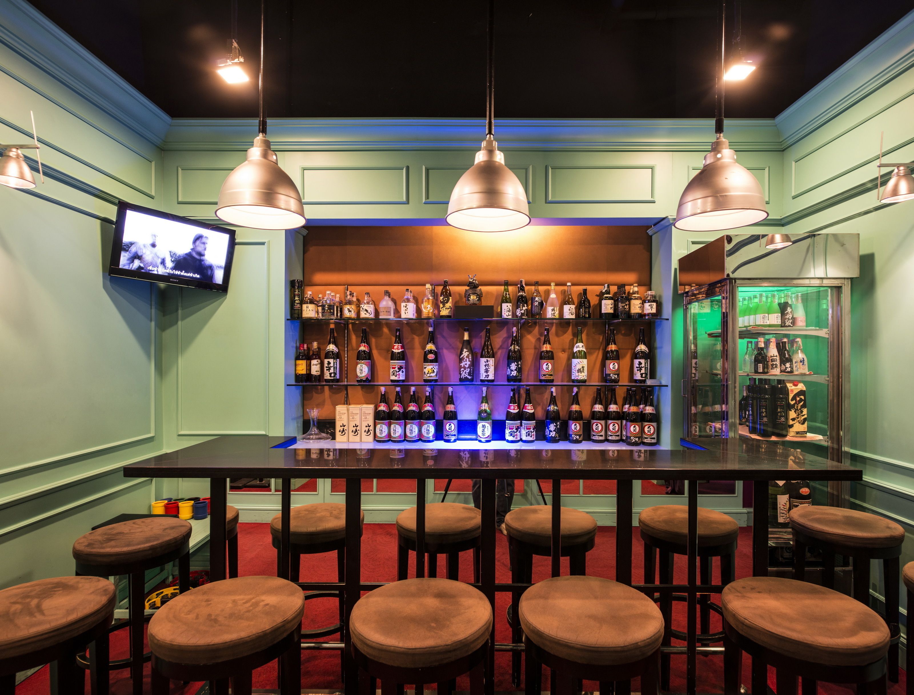 Een barruimte met meerdere barkrukken, een bar en flessenkasten.