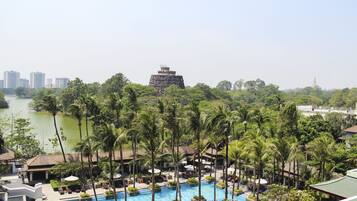 Relax by the resort's large pool surrounded by palm trees and lounge chairs, with a scenic view of the nearby water and distant buildings.