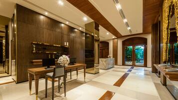 A modern hotel lobby with a reception desk, seating area, and a large mirror reflecting the space.