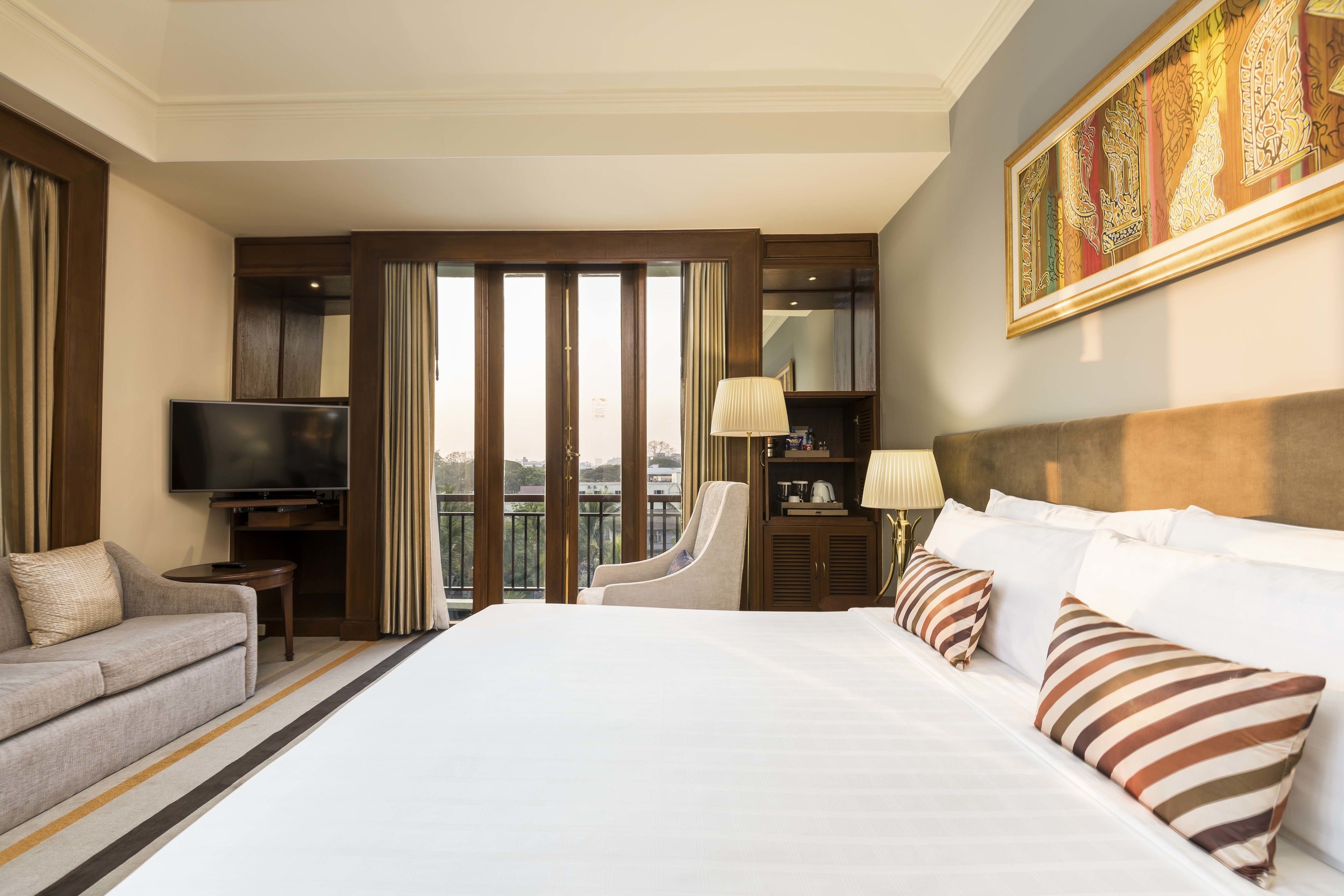 Habitación de hotel con una cama grande, un sofá, un televisor, una lámpara y un cuadro en la pared.