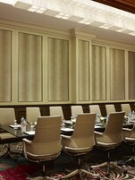 Un salón de conferencias con una larga mesa, varias sillas, botellas de agua y un arreglo floral.