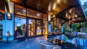 An outdoor seating area with wicker furniture and a glass enclosure with interior lighting. - Chatrium Hotel Royal Lake Yangon (Yangon)