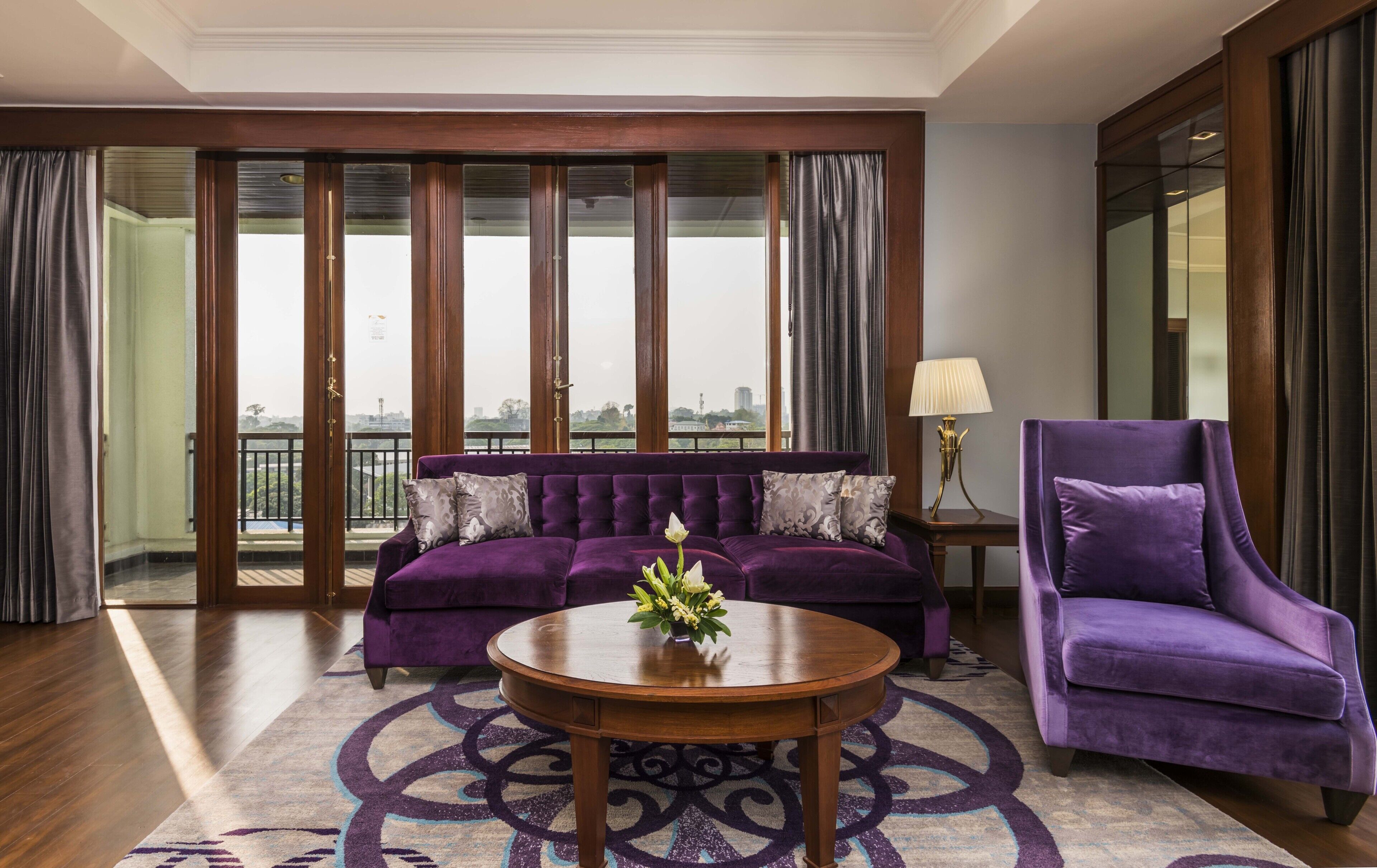 A living room with a purple sofa, a purple armchair, and a round wooden coffee table.