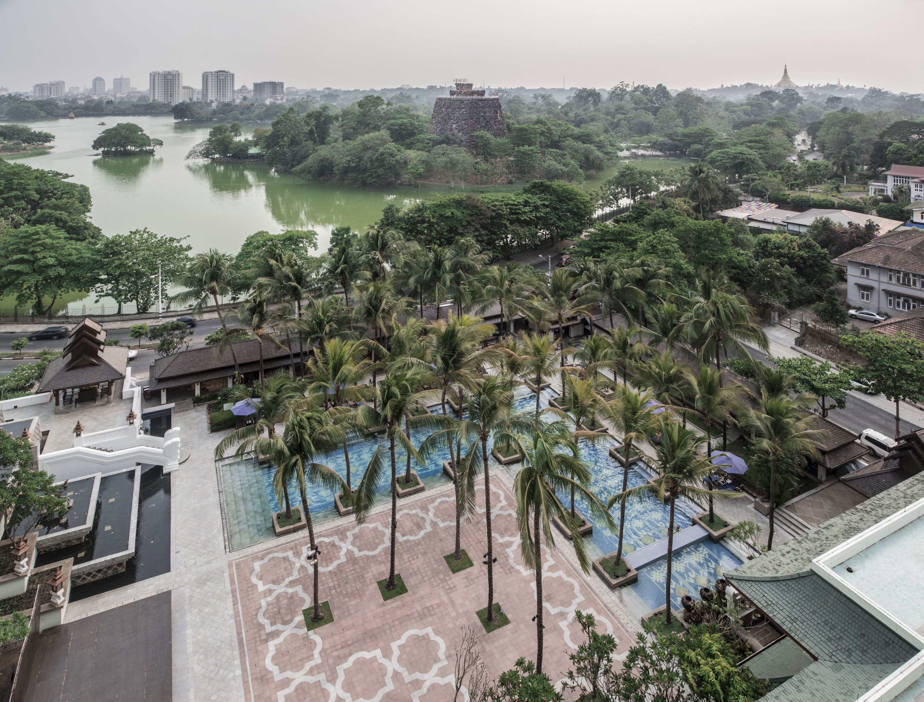 A resort with a swimming pool surrounded by palm trees, a view of a river, and a temple in the background.