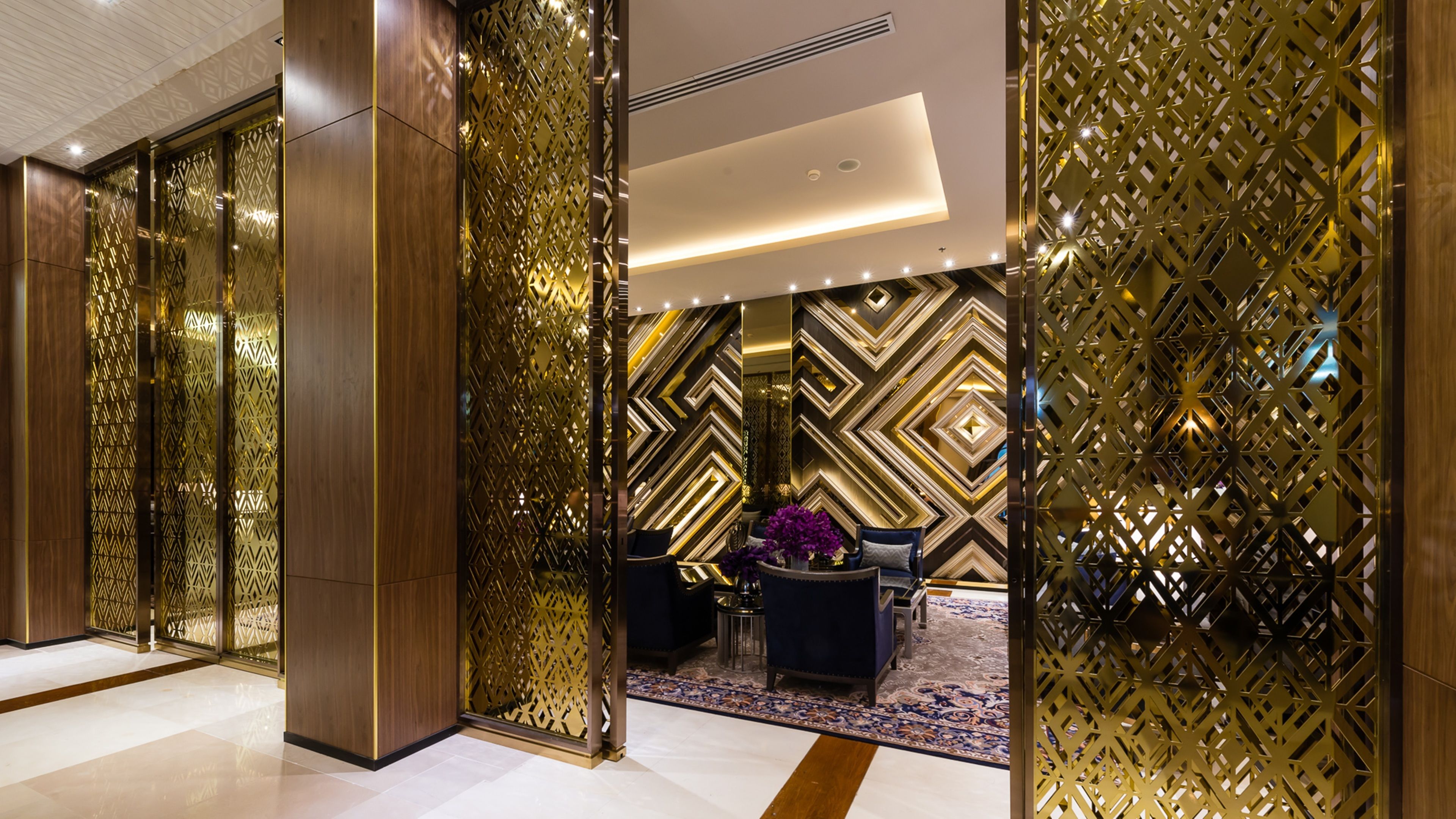 A modern lobby with geometric patterned walls, a reception desk, and a seating area with a patterned rug.