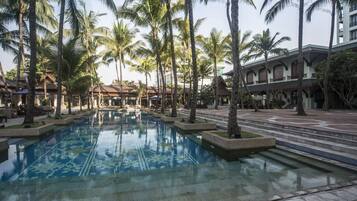 Ein Hotelpool, umgeben von Palmen und Gebäuden mit einem gefliesten Weg.