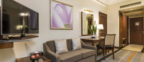 Habitación de hotel con televisión de pantalla plana, sofá, escritorio con lámpara y una silla.