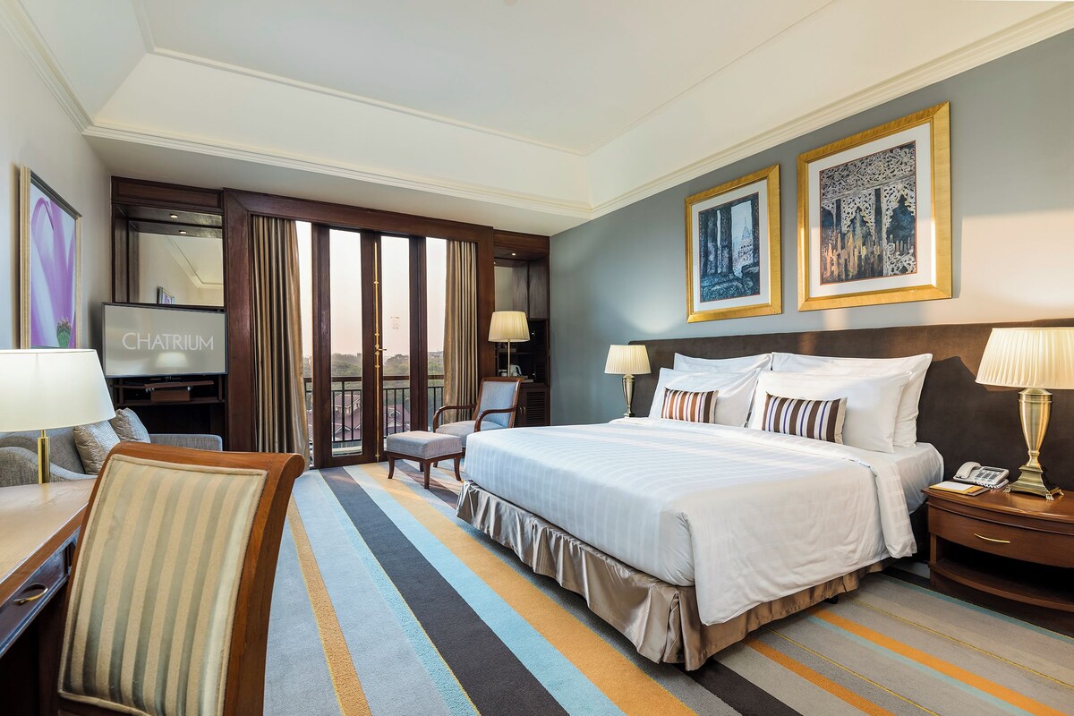 A hotel room with a large bed, a desk, a chair, a TV, and two framed pictures on the wall.