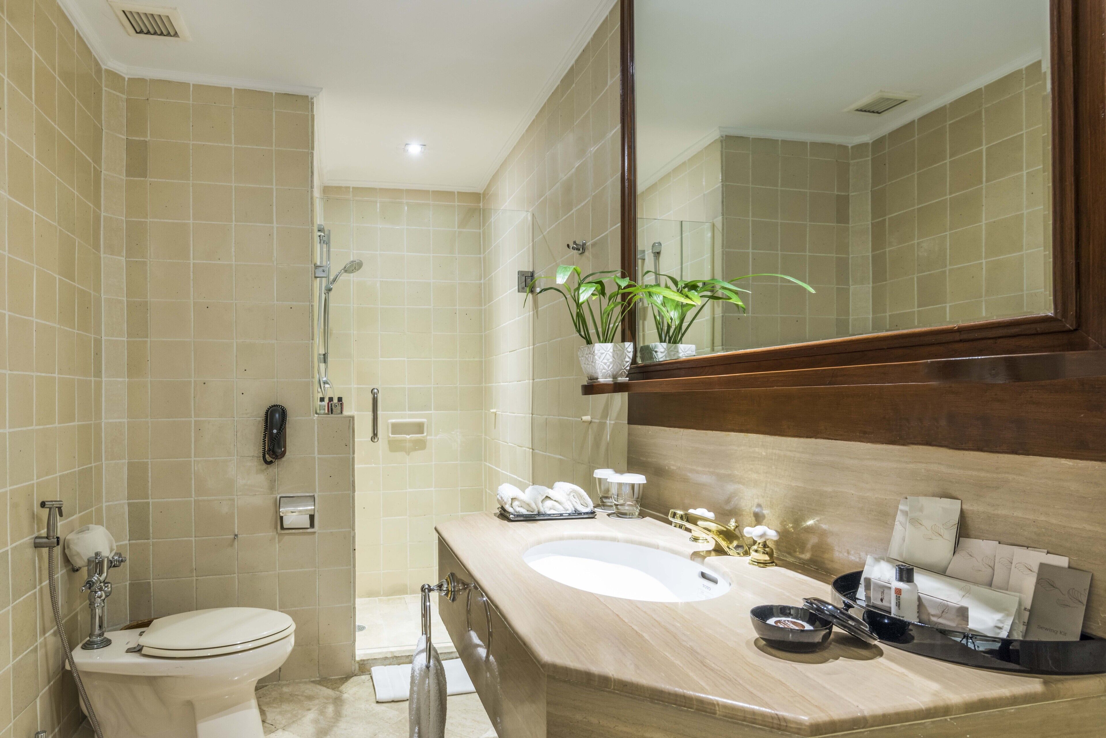 A bathroom with beige tiles, a white toilet, a sink with toiletries, and a mirror.