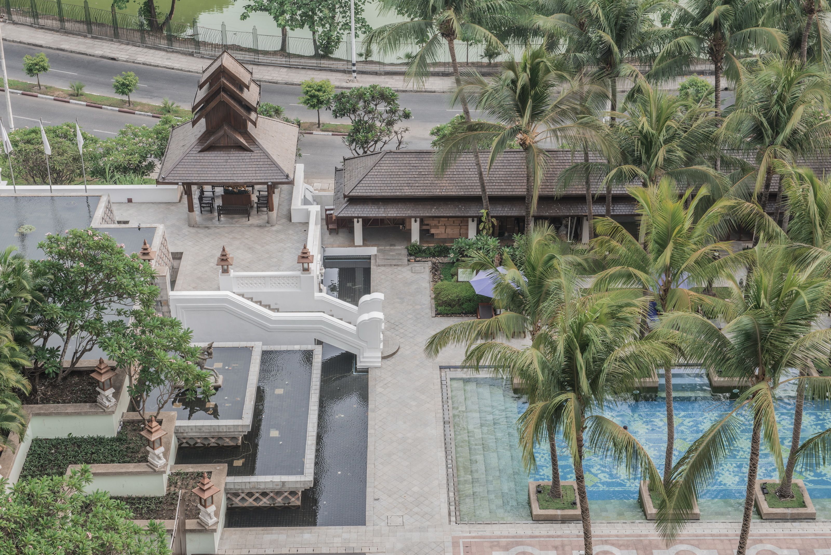 Vista aérea de un complejo turístico con piscina, palmeras y un pabellón tradicional.