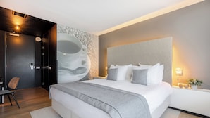 A modern bedroom with a large bed, a chair, a wall-mounted light, and a decorative wall piece.