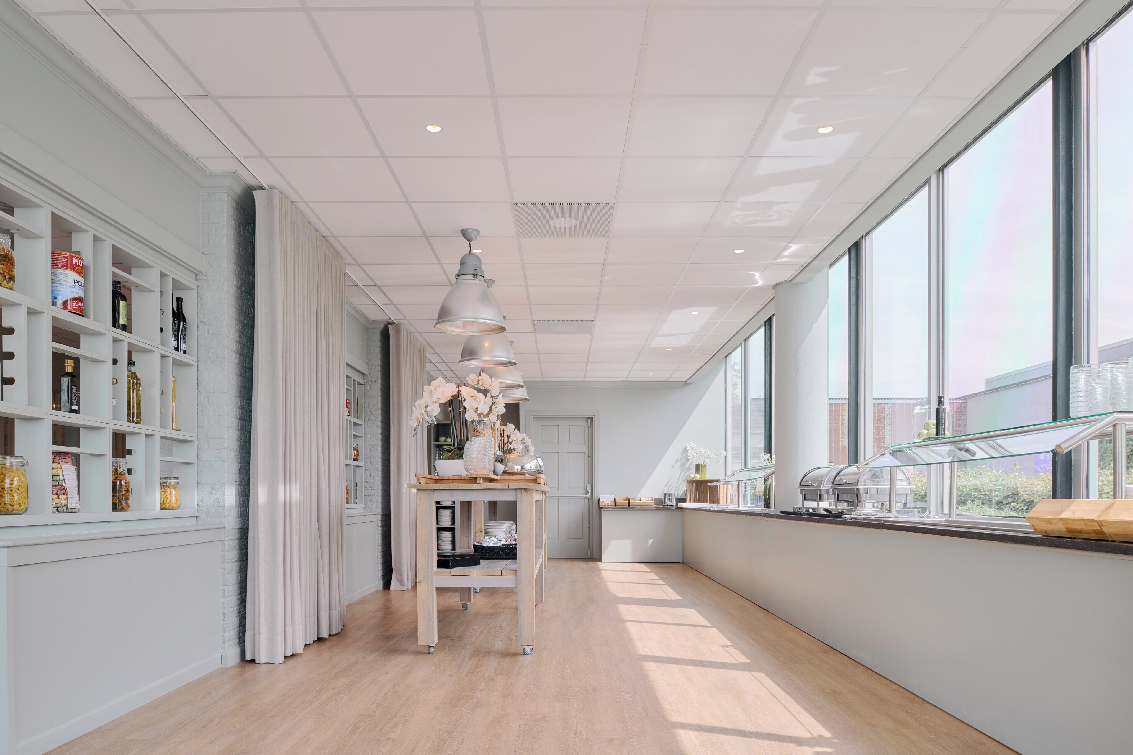 A modern kitchen with white cabinetry, a wooden countertop, and a large window providing natural light.