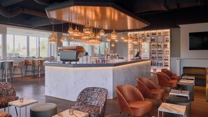 A modern bar area with a central counter, seating with round tables and chairs, and a wine display.