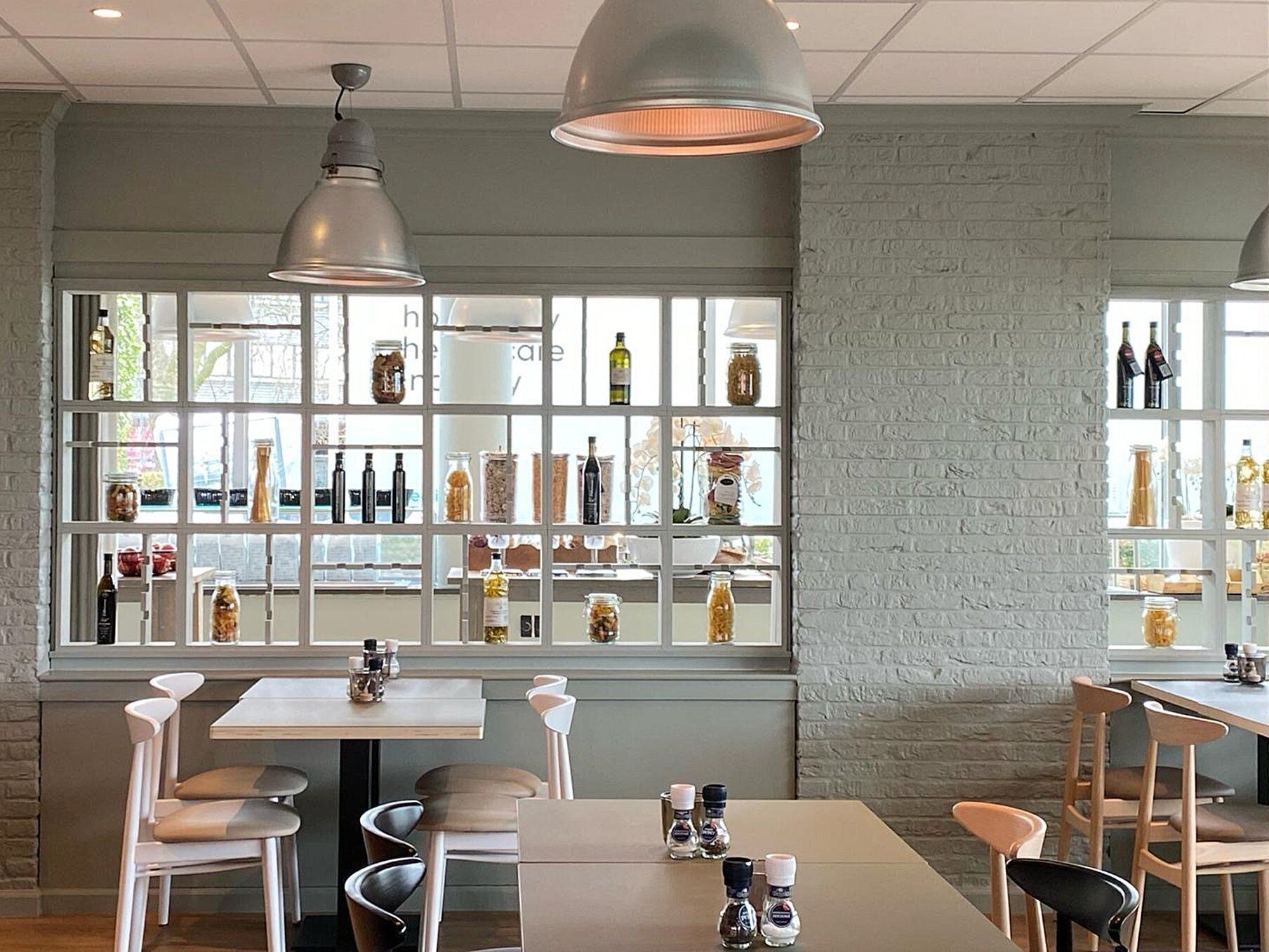 Interior de un restaurante con pared de ladrillo, amplias ventanas que muestran botellas e iluminación colgante.