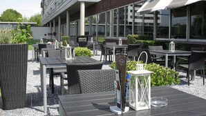 An outdoor seating area with tables and chairs, a sign for 'Dreamz Restaurant & Bar', and a modern building in the background.