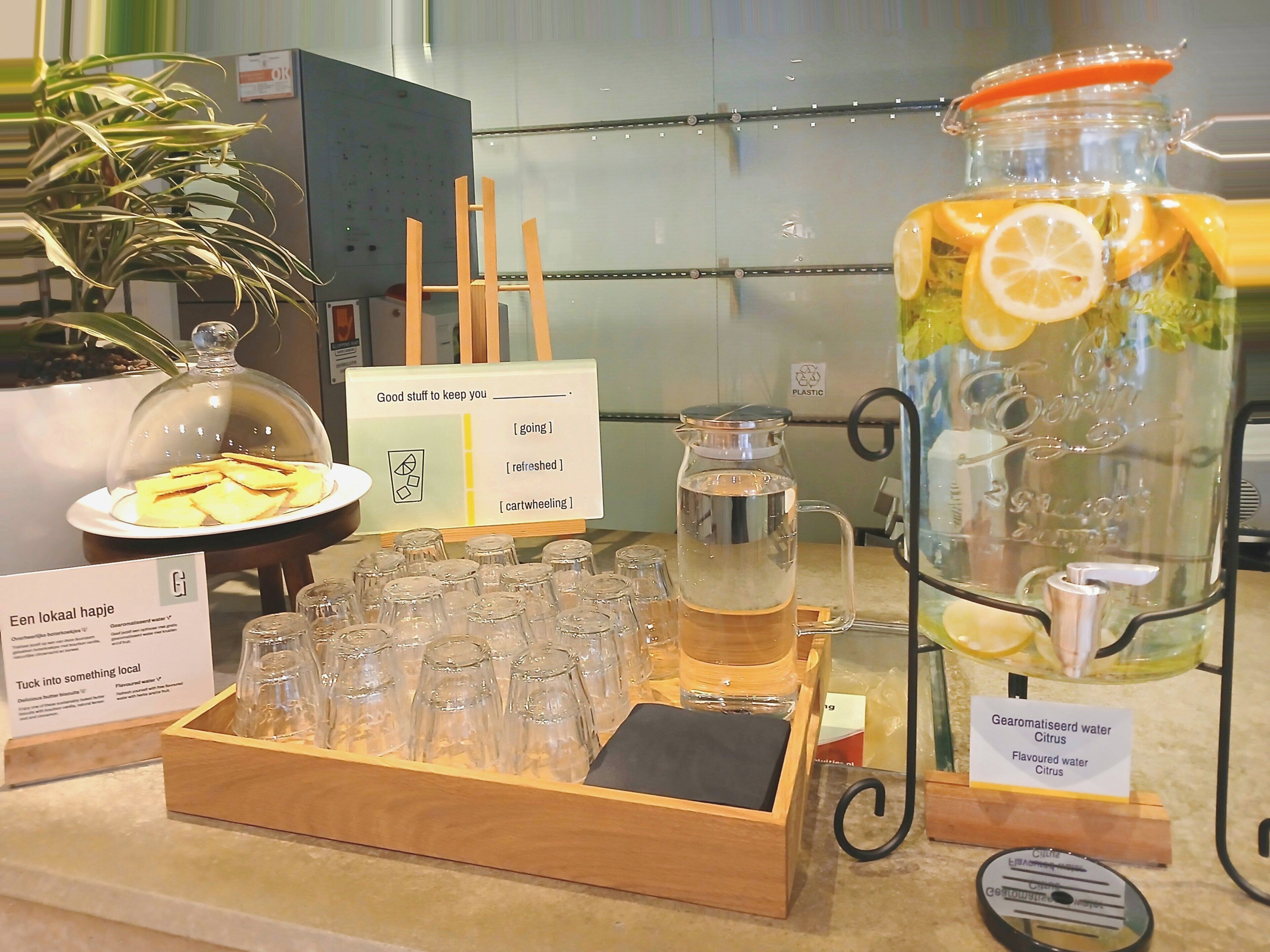 A beverage station with a pitcher of flavored water, a glass jar with lemon slices, and a tray of glasses.