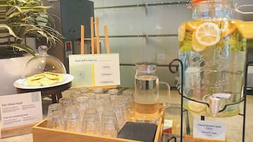 A beverage station with a pitcher of flavored water, a glass jar with lemon slices, and a tray of glasses.