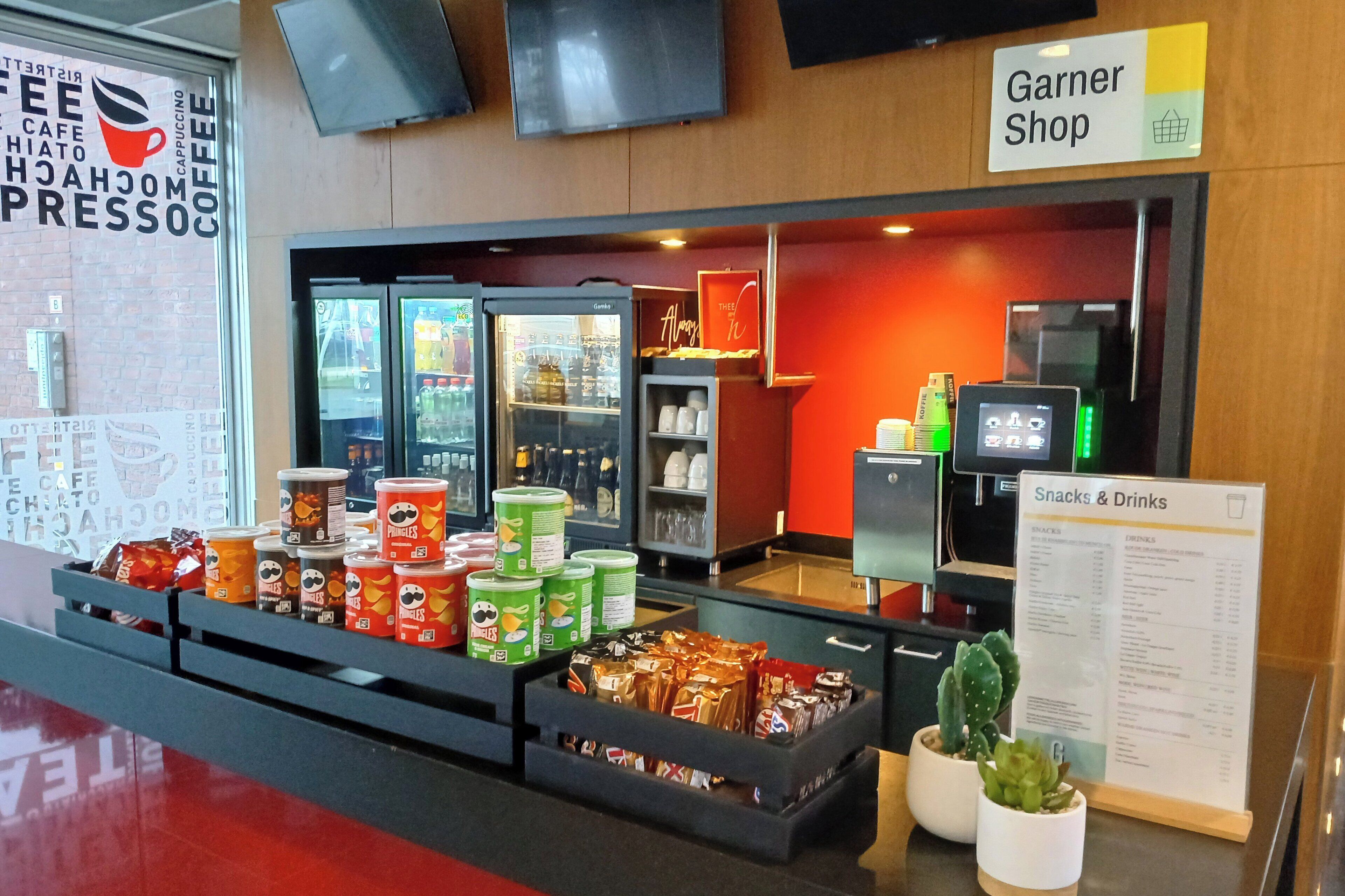 A snack and drink kiosk with a variety of packaged snacks and drinks, a cash register, and a menu sign.