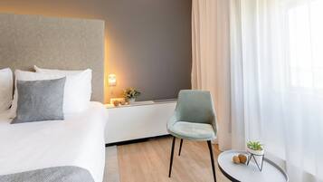 Una habitación de hotel con una cama, una silla, una mesita con una planta y una mesita de noche con una lámpara.