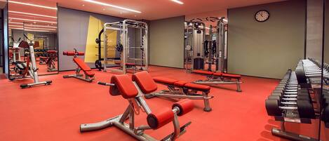 A gym with red flooring, weightlifting equipment, and a clock on the wall.