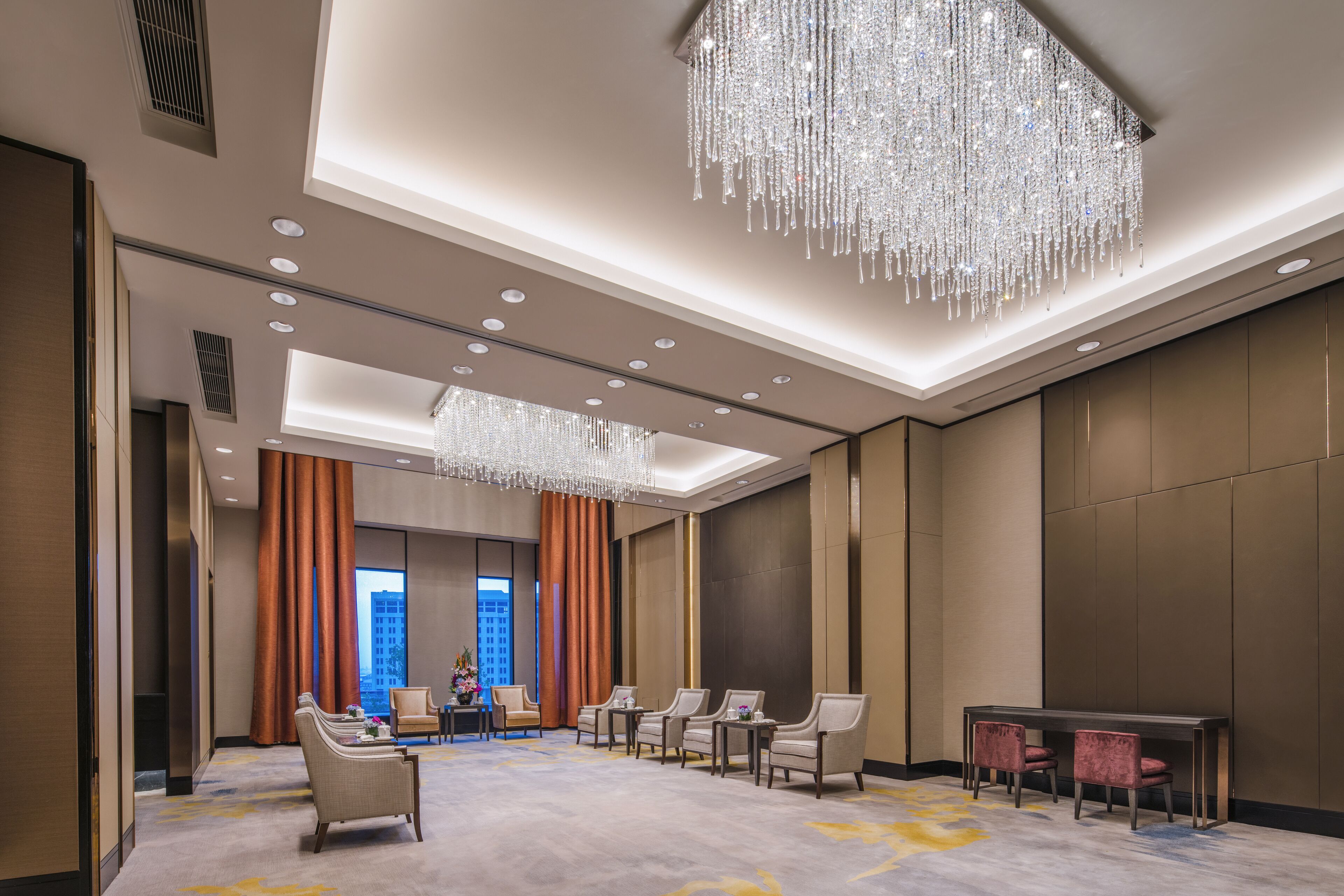 Um amplo hall de hotel com um lustre grande, área de estar e vista para a paisagem urbana através de janelas amplas.