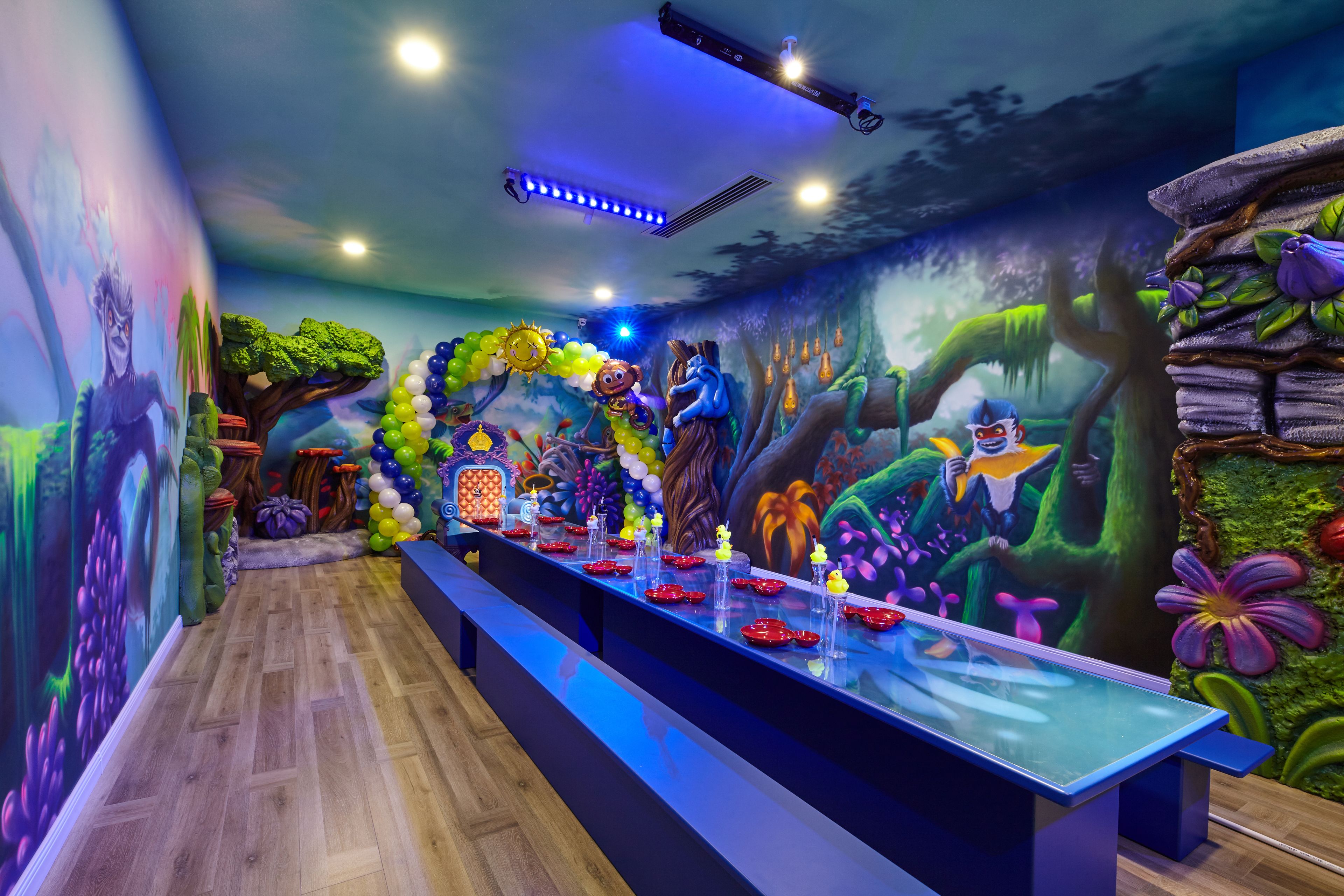 A room with a long table, colorful murals, and a ceiling with lights.
