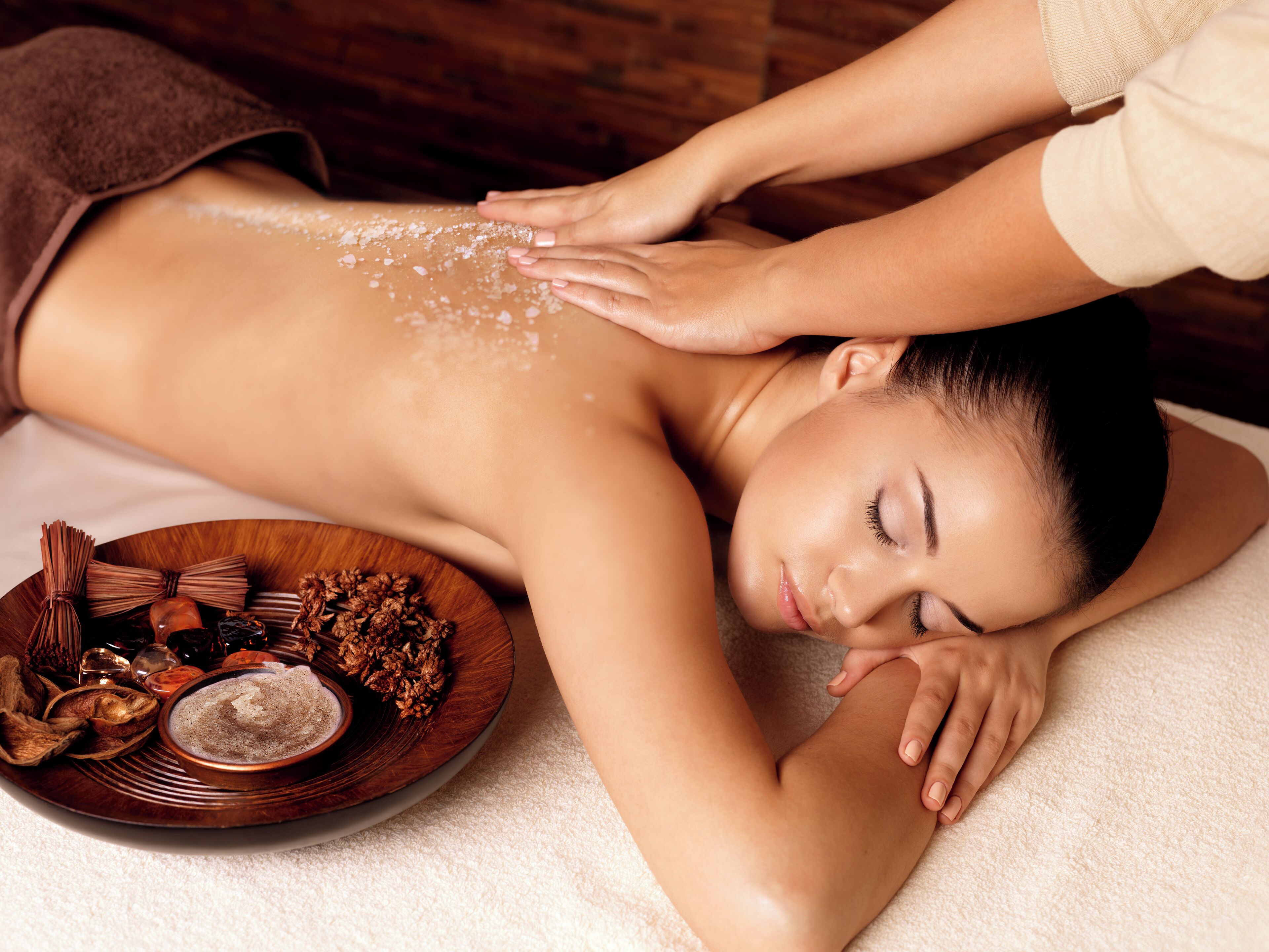 A person receiving a back massage with a tray of spa products nearby.