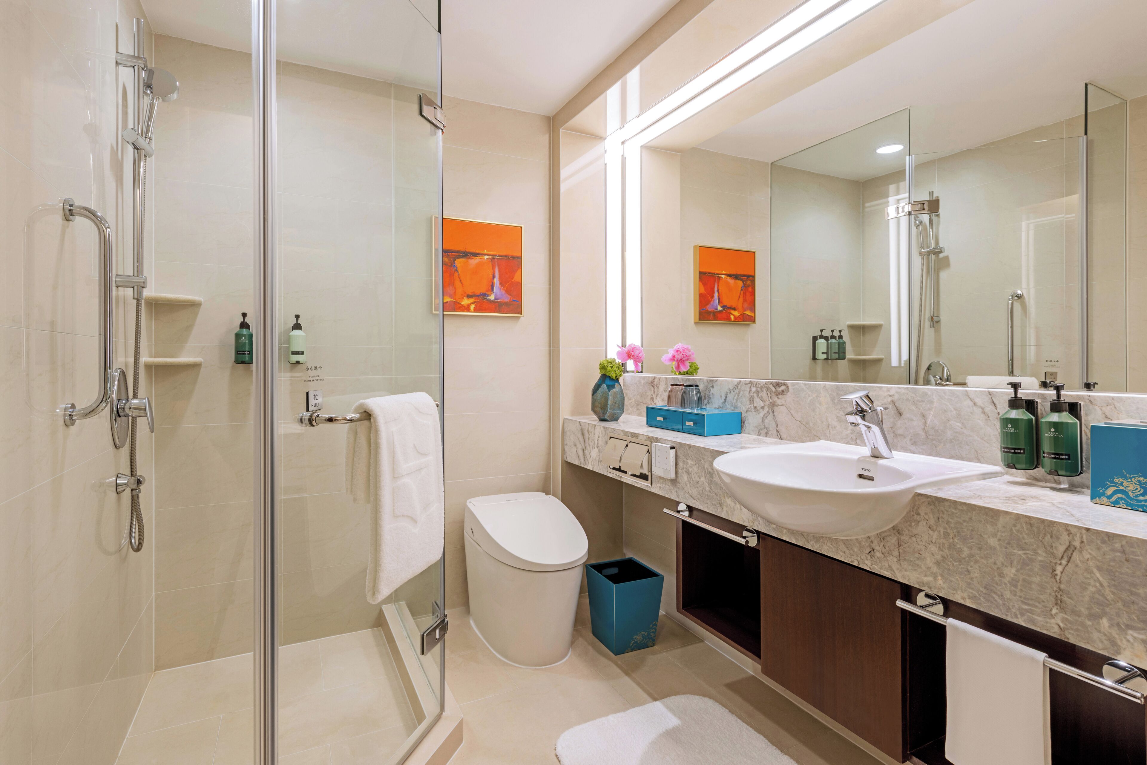 Un baño moderno con ducha de vidrio, inodoro blanco, lavamanos con encimera de mármol y un espejo grande.