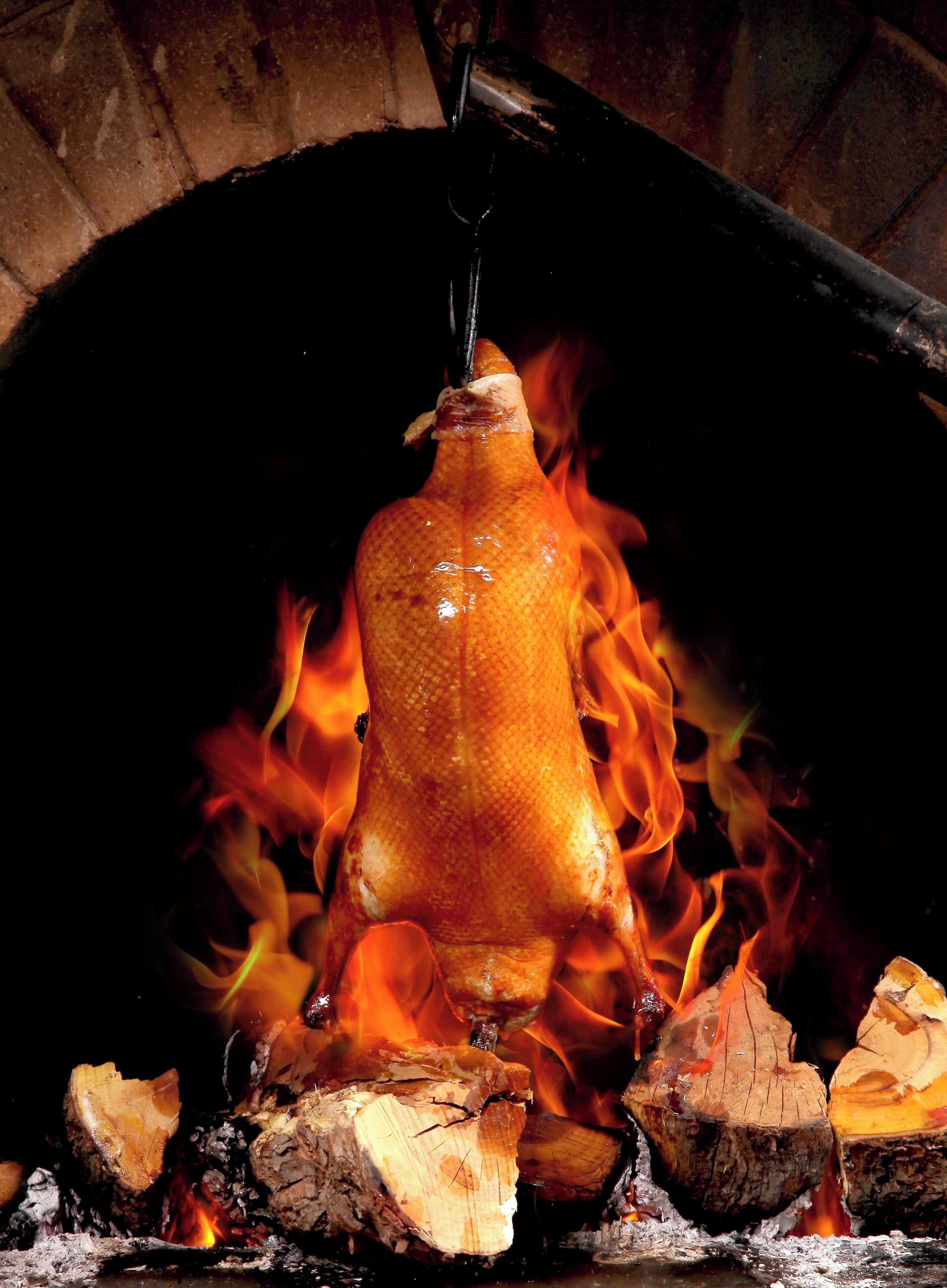 Ein gebratenes Schwein hängt über dem Feuer in einem Backofen aus Ziegeln.