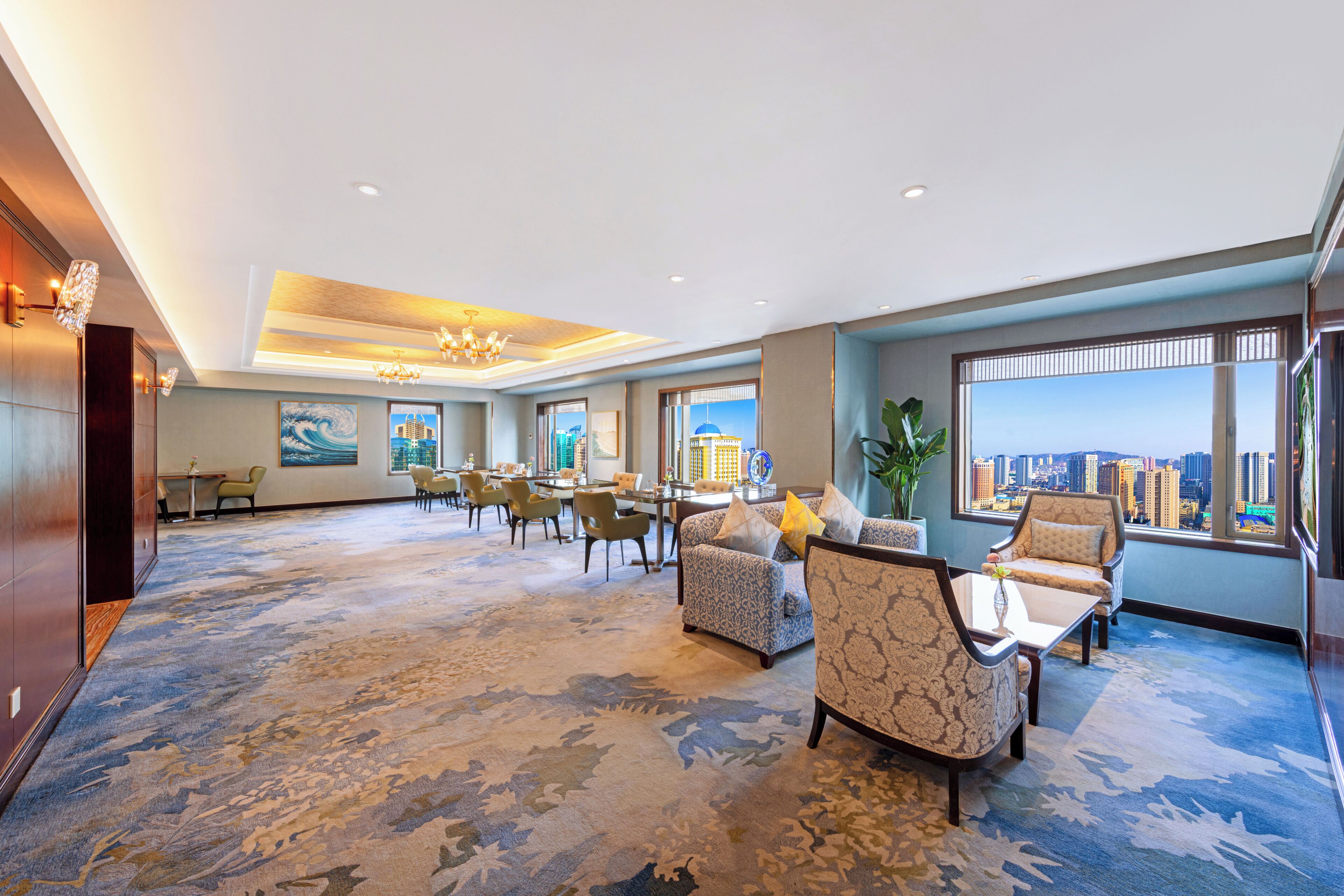 A spacious lobby with a high ceiling, modern furniture, and large windows offering a city view.