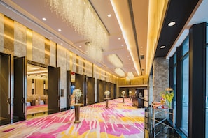 A spacious hotel lobby with a vibrant carpet, elegant chandeliers, and a reception area with a counter and flowers. - Shangri-La Dalian (Dalian)
