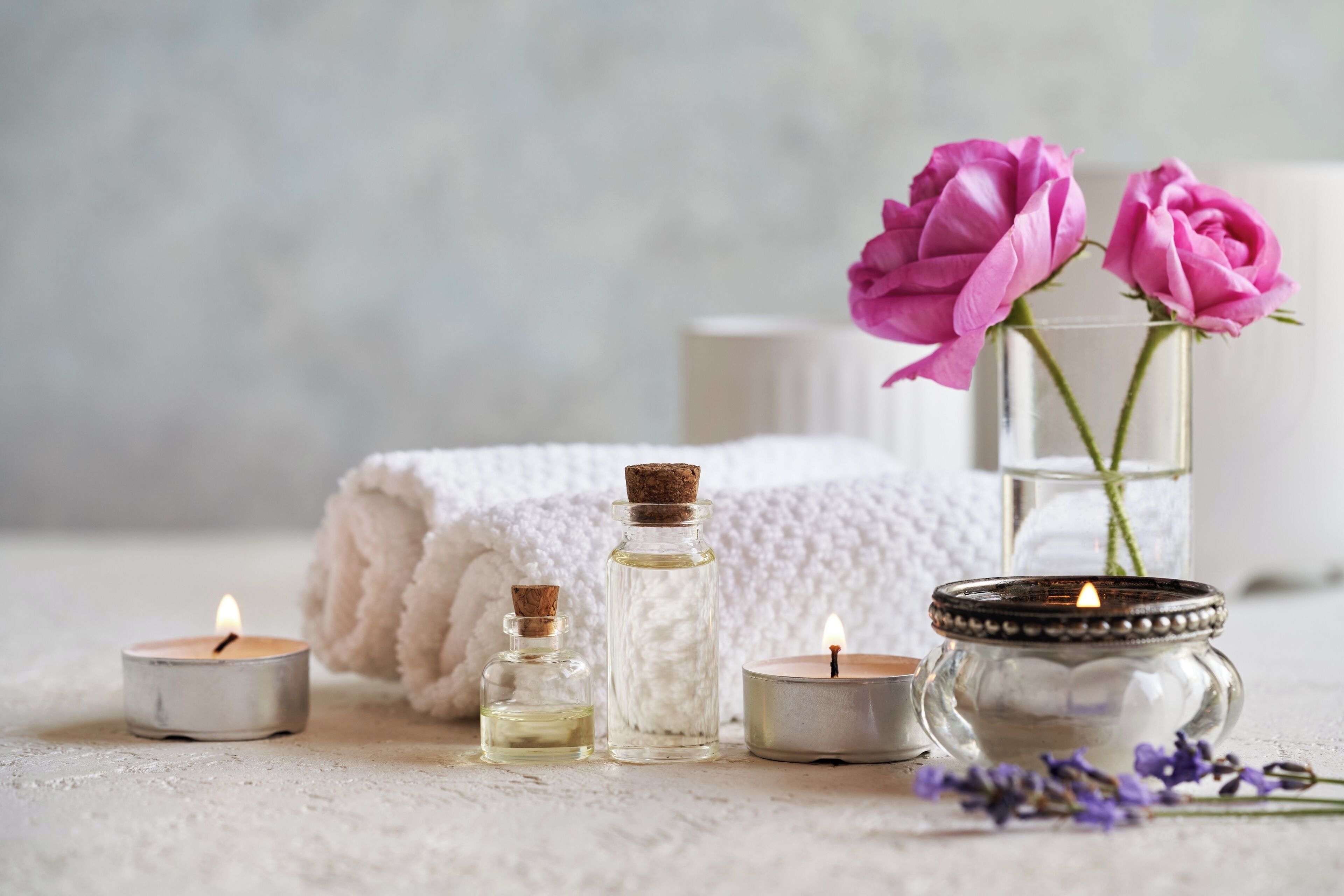 Une bougie, une bouteille en verre, un bocal et un vase avec des fleurs, le tout posé sur une surface texturée.