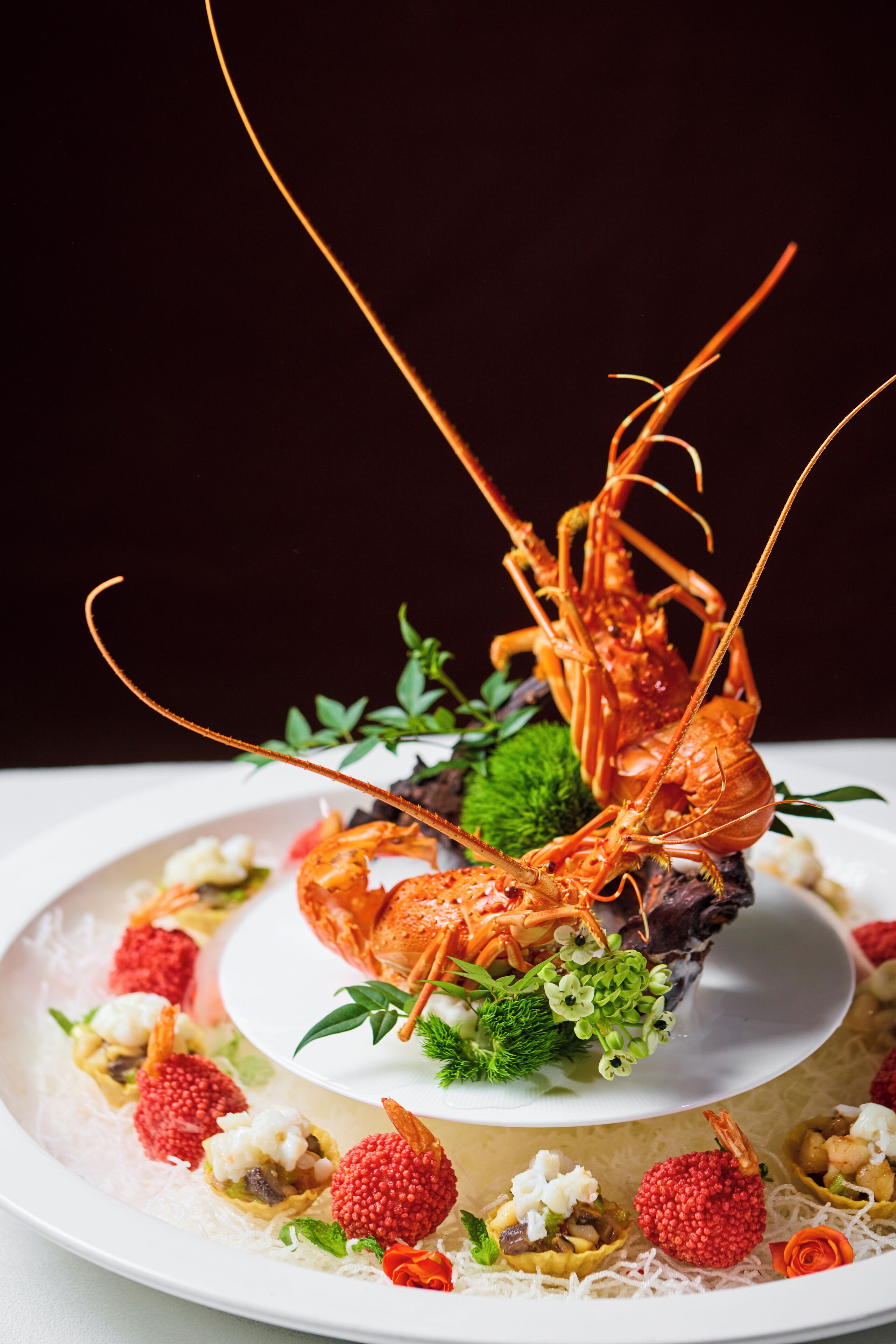 Plato de mariscos con un langostino como pieza central, decorado con hierbas y pequeñas bayas rojas.