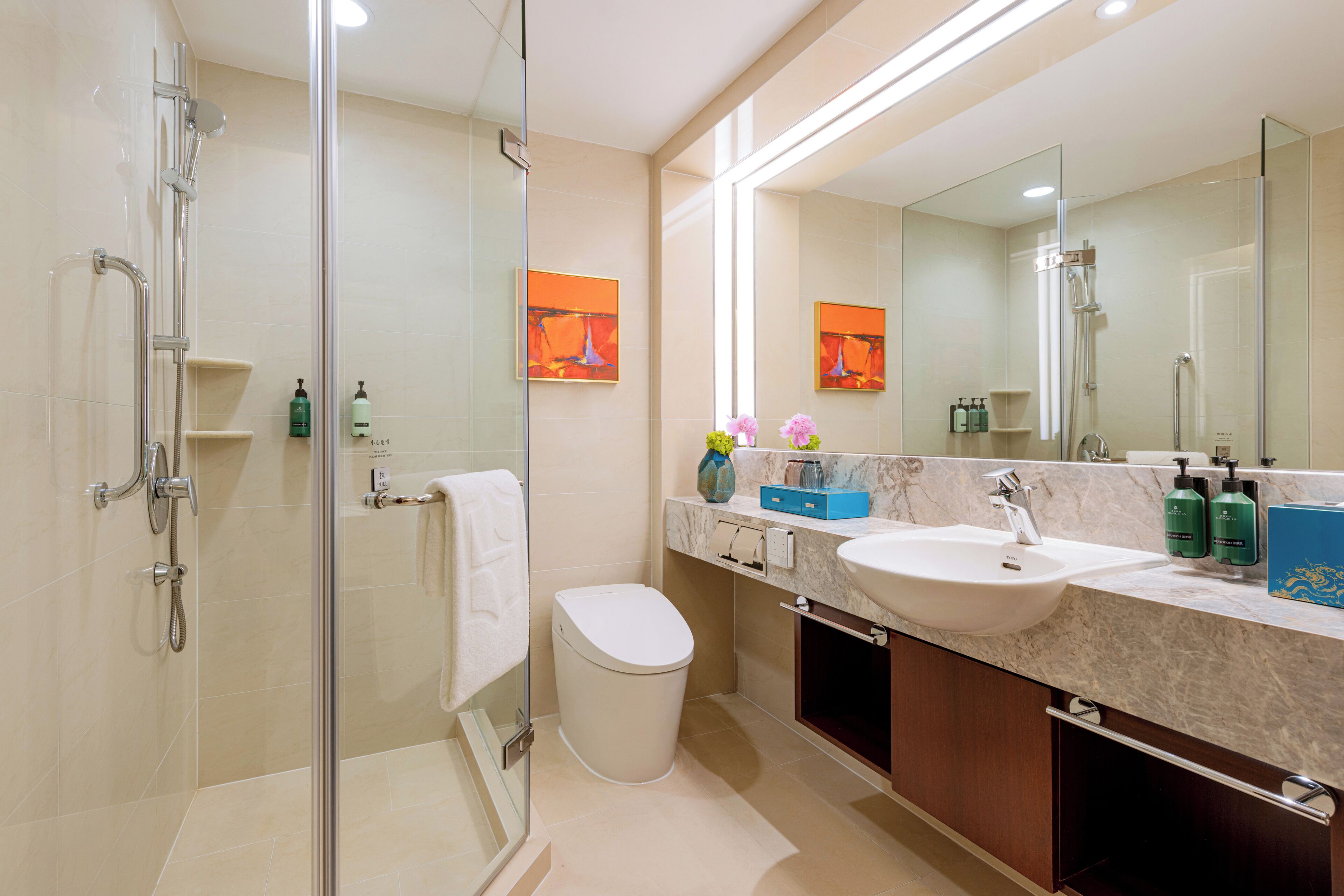 A modern bathroom with a glass-enclosed shower, a white toilet, a sink with a marble countertop, and a large mirror.