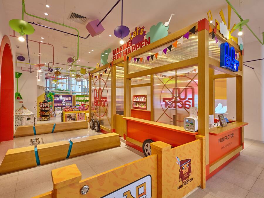 A colorful indoor play area with a 'Fun Factor' sign, play structures, and a counter with a computer.