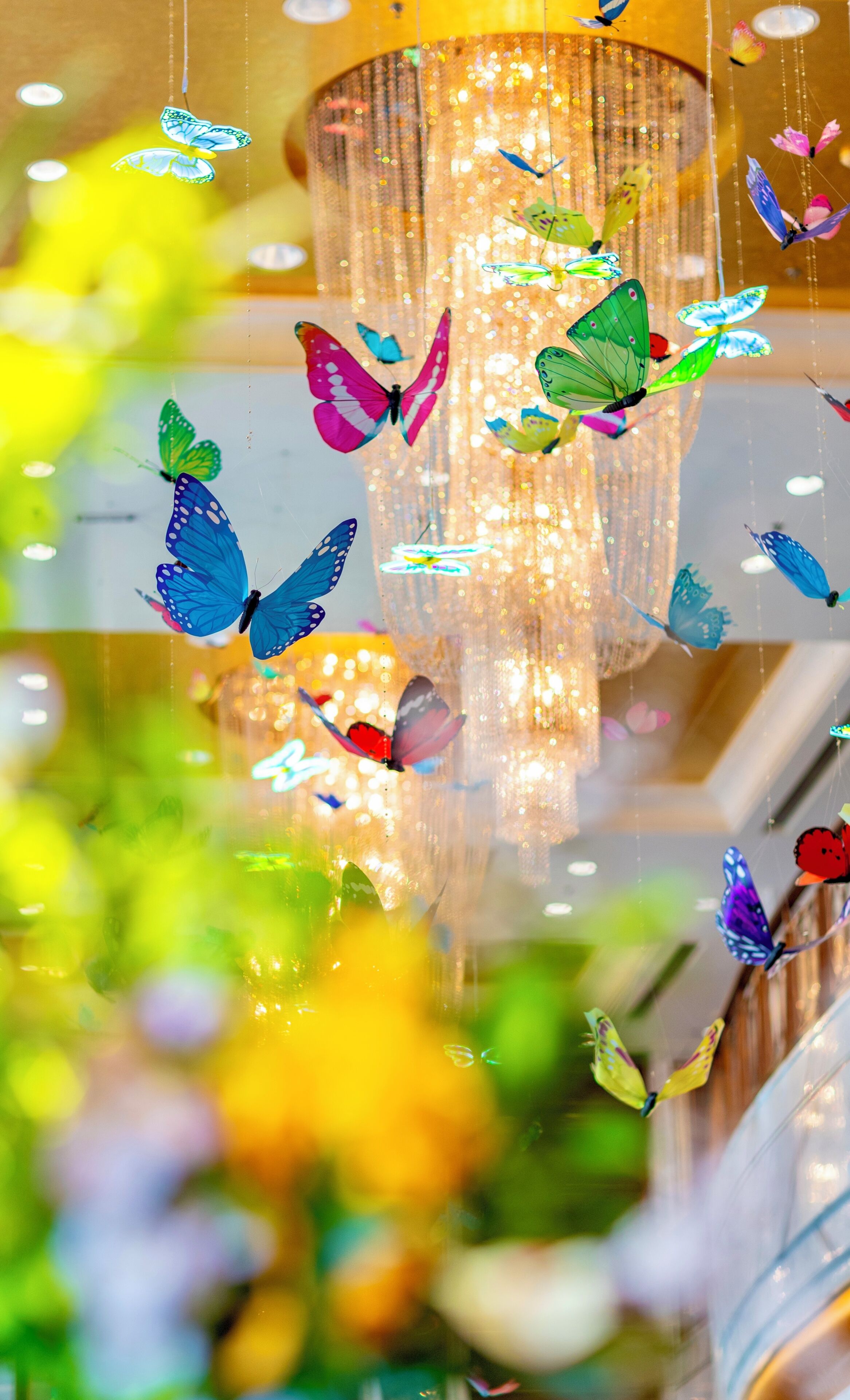 A chandelier with hanging butterflies and a blurred background of greenery.