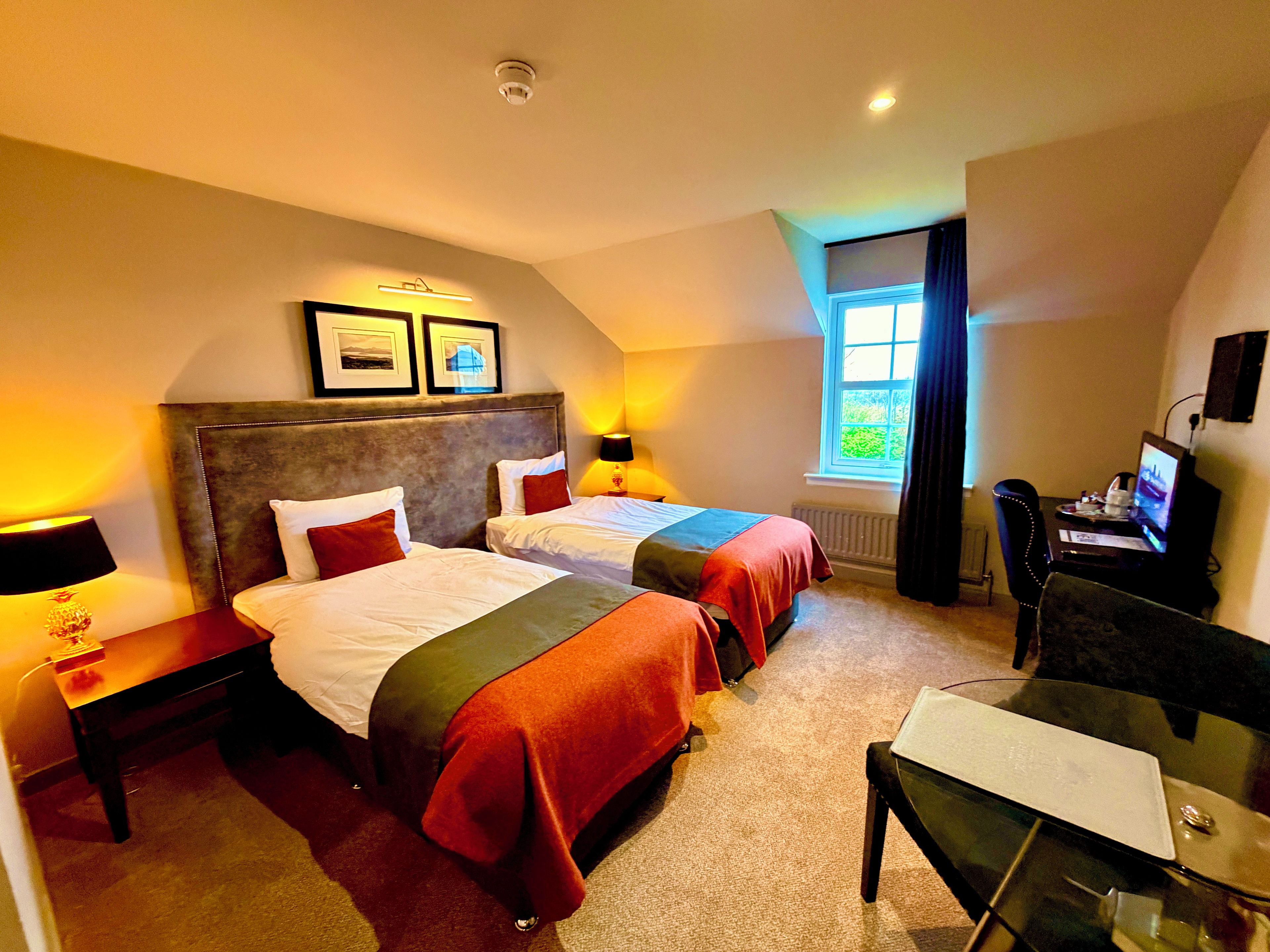 A hotel room with two beds, a desk with a computer, a chair, and a window with curtains.