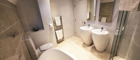 A modern bathroom with a bathtub, two sinks, a toilet, and a glass shower enclosure.