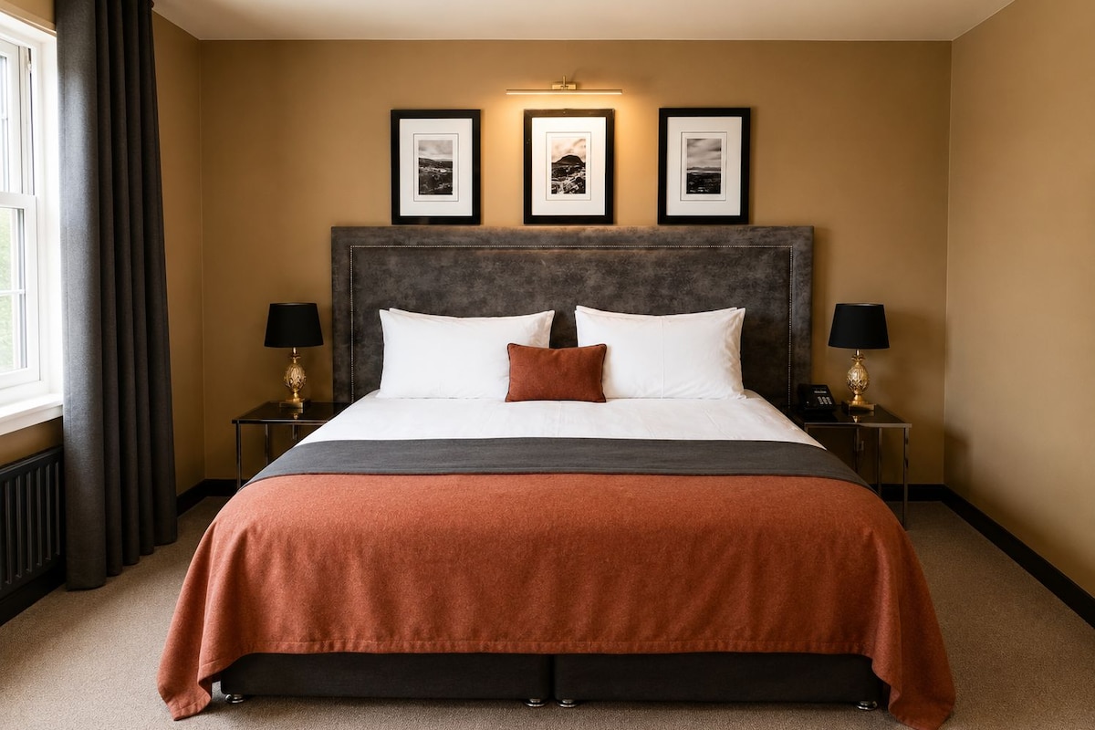 Quarto de hotel com uma cama grande, duas mesas de cabeceira com luminárias e três quadros na parede.