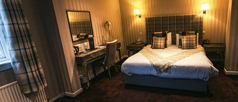A hotel room with a large bed, a desk with a chair, a small table, a mirror, and two bedside lamps.