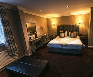 Habitación de hotel con una cama grande, un escritorio con silla, una mesita pequeña, un espejo y dos lámparas de noche.