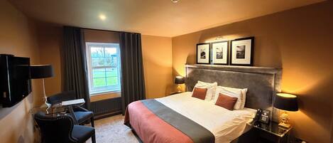 Una habitación de hotel con una cama grande, un escritorio con silla, un televisor y un ventanal con cortinas.