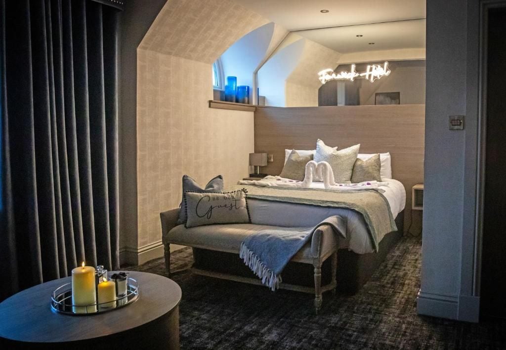 A hotel room with a bed, bedside table, and a wall-mounted shelf with decorative items.