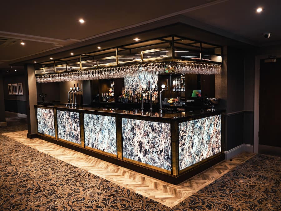 A bar area with a marble countertop, multiple bottles, glasses, and a television screen.