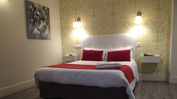 A neatly made bed with red and white bedding, two bedside lamps, a telephone, and a small bedside table. - Hôtel le Dauphin (Puteaux)
