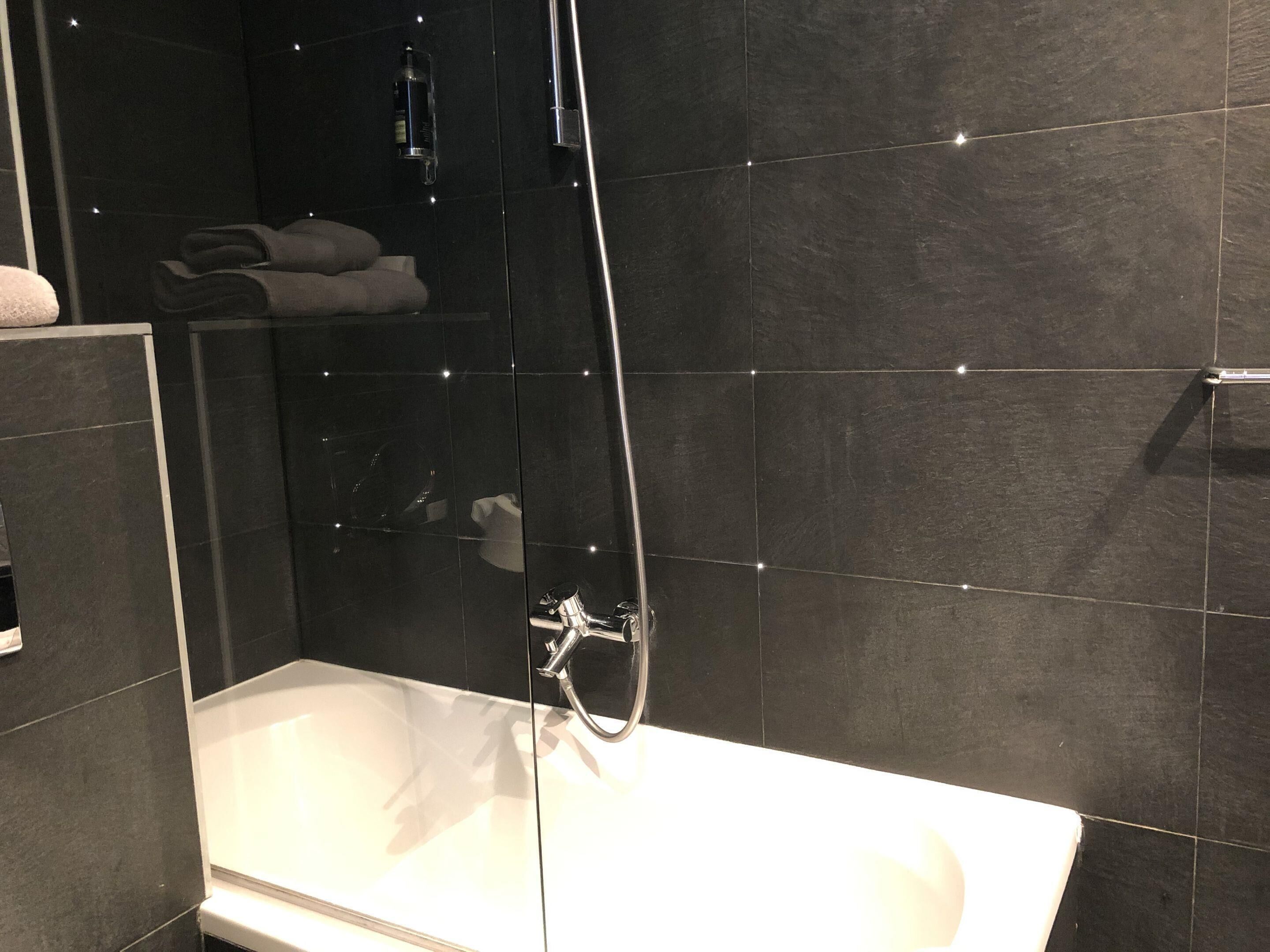 Een moderne badkamer met een douchecabine van glas, een witte badkuip en donker betegelde wanden.