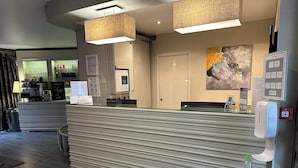 A hotel reception area with a counter, a hand sanitizer dispenser, and a painting on the wall. - Hôtel le Dauphin (Puteaux)