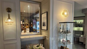 A dining area with a round table, chairs, a vase with flowers, a wine rack, and a glass display case with Eiffel Tower models. - Hôtel le Dauphin (Puteaux)