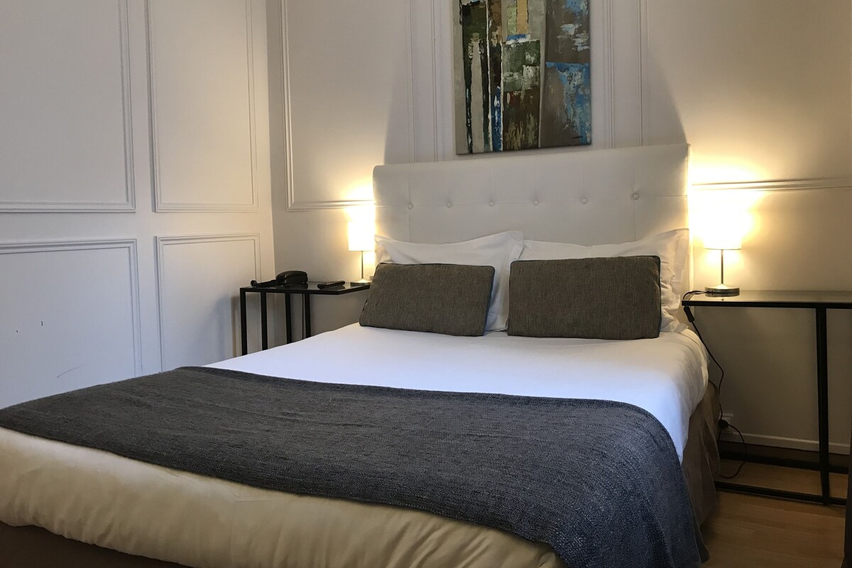 Ein Hotelzimmer mit einem großen Bett, zwei Nachttischen, einer Bettseite mit einem Gemälde und zwei Wandlampen.
