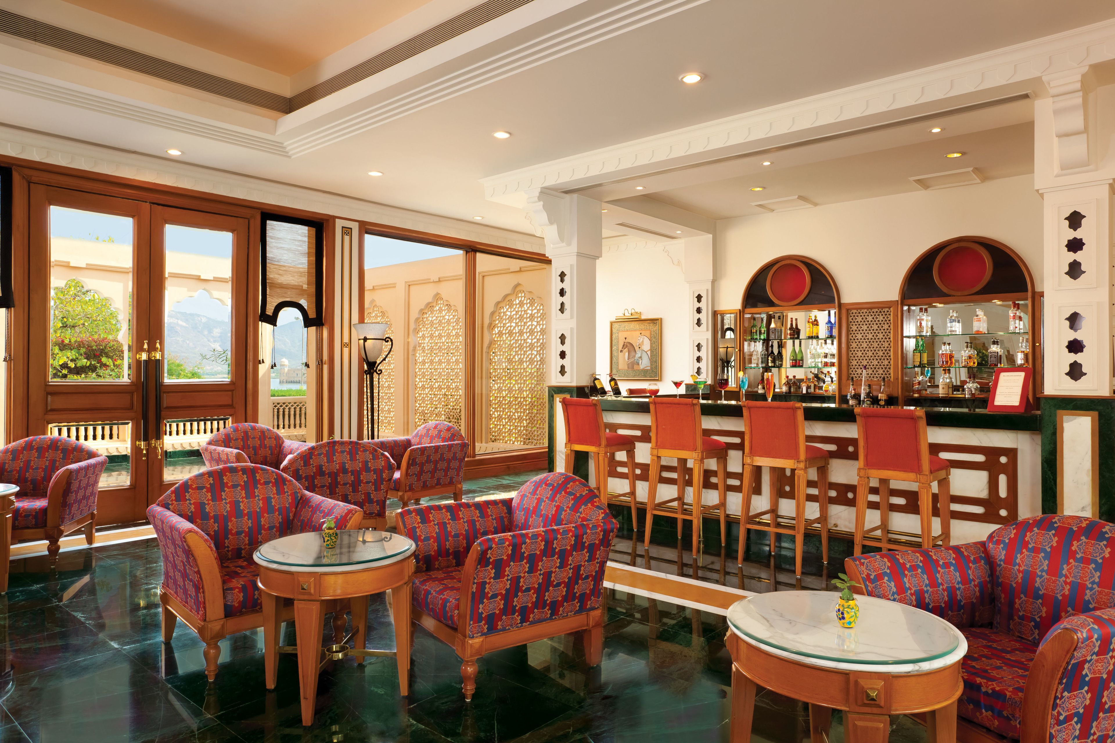 A hotel lobby with patterned chairs, a bar area, and a view of mountains through large doors.